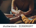 Small photo of Christian family sitting around a wooden table with open bible page and holding hands to bless and pray for each other. comforting and praying together.Christians and Bible study concept.