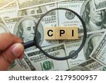 Small photo of CPI, consumer price index symbol. hand holding magnifying glass investigating wooden block with words CPI, consumer price index on dollar bills. Business and CPI, consumer price index concept.