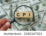 Small photo of CPI, consumer price index symbol. hand holding magnifying glass investigating wooden block with words CPI, consumer price index on dollar bills. Business and CPI, consumer price index concept.