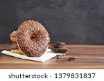 On a dark wooden surface with a black background donuts are stacked, one leaning against the pile. This is covered with chocolate pieces. Concept of delicious fresh donuts with chocolate beside it