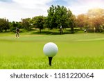 White Golf ball on tee ready to be shot on blurred beautiful landscape of golf course in bright day time with golfer playing golf on course. Sport, Recreation, Relax in holiday concept.	