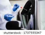 Medical worker in N95 PPE performing nasal throat swab on person in vehicle through car window,COVID-19 UK mobile testing centre drive thru facility,hands closeup in blue gloves holding test kit