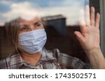 Small photo of Portrait of elderly senior citizen wearing face mask looking through room window,Coronavirus COVID-19 pandemic outbreak nursing home crisis,high mortality rate and death cases among older population