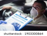 Small photo of Male driver wearing protective N95 face mask sitting by the wheel in drive-thru COVID-19 test centre or border crossing,health check up questions,medical worker ticking off symptoms on clipboard form