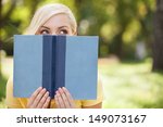 Smart beauty. Beautiful young women holding book in front of her face and looking out of it while relaxing in park