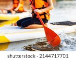 woman in life jacket sit at sub board at river ar evening , forest trees background