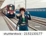 Young beautiful woman waiting on a train station platform and taking selfie with a smartphone. Woman with afro hair using smartphone while standing on the railway station platform.