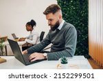 Elegant young businessman analyzing data in office and sitting at the desk and using a computer. Thoughtful businessman thinking of online project looking at laptop at workplace.