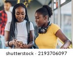 Happy african american female friends standing in a bus and using a smartphone while riding a bus. Public transportation. Black woman friends traveling to work and chatting during their trip.