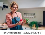 Portrait of a happy senior woman cooking in her modern kitchen and chopping fresh vegetables for salad at kitchen table. Copy space. Cheerful elderly homeowner woman cooking for her family.