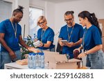 Small photo of Multiracial volunteers working at charity organization and wearing blue t shirt while packing food grocery in donations box. Volunteering, social help for poor and needy. Copy space.