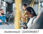 Small photo of African american woman wearing earphones and smiling at a message on her smartphone while riding a bus. Black woman catching up on social media while in a bus during her morning commute. Copy space.