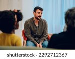 Small photo of Portrait of a sad young man talking about his problems during a meeting at mental health center. Group therapy participants sitting in a circle and talking. Mental health concept. Copy space.