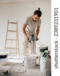 Small photo of Full length of a house painter mixing plastering materials with a manual cement mixer while standing in a house in renovation process. A builder is preparing plaster for plastering and skim coating.