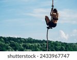 Small photo of Rear view of a woman athlete partake in one of the events of an obstacle course race while climbing the rope. Female working out outside. Sport competition and OCR race.