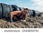 Small photo of Portrait of a woman athlete partake in one of the events of an obstacle course race while crawling out of the tunnel made of car tires. Female working out outside. Sport competition and OCR race.
