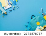 Small photo of Top view photo of backpack notebooks pencil-case scissors drink bottle plastic alphabet letters binder clips plane shaped sharpener pens adhesive tape stapler ruler calculator isolated blue background