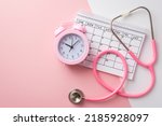 Small photo of Breast cancer awareness concept. Top view photo of pink alarm clock calendar and stethoscope on bicolor pastel pink and white background
