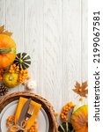 Small photo of Thanksgiving day concept. Top view vertical photo of rattan basket with plate knife fork napkin pumpkins pattypan pine cone maple leaves rowan on isolated white wooden table background with copyspace