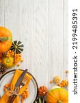 Small photo of Thanksgiving day concept. Top view vertical photo of plate knife fork napkin raw vegetables pumpkins pattypans pine cone and rowan berries on isolated white wooden table background