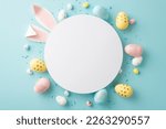 Easter decor concept. Top view photo of white circle easter bunny ears yellow blue pink eggs and sprinkles on isolated pastel blue background with blank space