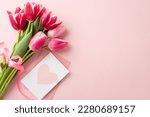 Small photo of Mother's Day concept. Top view photo of bouquet of pink tulips tied with silk ribbon and envelope with postcard on isolated pastel pink background with copyspace