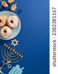 Small photo of Stylish Hanukkah table arrangement. Top view vertical image of traditional Jewish meal - sufganiyot, Star of David, menorah, and dreidel game on blue background, space for text or advertising