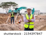 Small photo of Construction engineer wear safety uniform under inspection and survey workplace by radio communication with excavation truck digging, theodolite and worker construction road background.