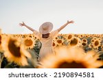 Unrecognizable woman with open arms in sunflowers field. Yellow colors, warm toning. Free girl in straw hat and retro dress. Vintage timeless fashion, amazing adventure, countryside, rural scene