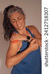 Small photo of brunette woman in sports clothes winces in pain touching her shoulder which is reddened and hurts, she has an injury. white background