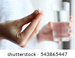 white pill and a glass of water in female hands. health concept