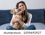 beautiful happy african american girl hugging teddy bear and smiling at camera on bed 