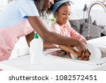 african american mother and daughter washing dishes with detergent on kitchen