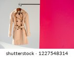 elegant beige trench coat on hanger at pink and grey background 