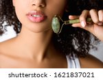 cropped view of african american girl using stone facial roller, isolated on grey