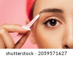 Small photo of cropped view of young woman with dyed hair holding tweezers while shaping eyebrow isolated on pink