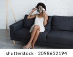 Smiling african american woman with clay mask on face talking on smartphone on couch at home