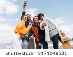 Small photo of asian skater showing rock sign near excited friends taking selfie outdoors