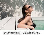 Small photo of happy young woman with wet hair and stylish sunglasses sunbathing in pool