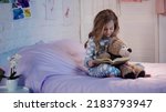 Small photo of Smiling kid in pajama reading fairytale near soft toy on bed in evening