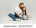 Bearded man in jeans and t-shirt kissing smiling preteen daughter on grey background