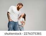Smiling man hugging daughter in t-shirt and jeans isolated on grey