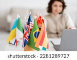 Small photo of selective focus of various international flags near blurred laptop and language teacher having online lesson at home