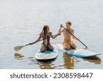 carefree african american woman and young, cheerful redhead man in colorful swimwear spending summer vacation on lake and sailing on sup boards with paddles