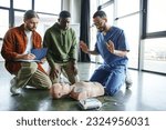 Small photo of young paramedic explaining cardiac resuscitation techniques to interracial participants near CPR manikin with automated external defibrillator, effective life-saving skills and techniques concept