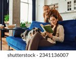 Woman reading book near boyfriend and border collie dog on vouvh in living room at home