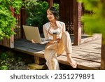 Small photo of happy indian woman in ethnic wear with laptop and takeaway coffee in wooden alcove in park