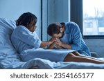 Small photo of miscarriage, depressed african american woman holding hand of grieving husband, hospital ward