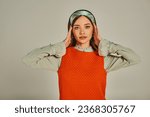 portrait of charming woman in orange dress adjusting colorful headband on grey, old-fashioned style