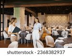 event coordinator with clipboard showing modern banquet hall with decorated tables to young woman